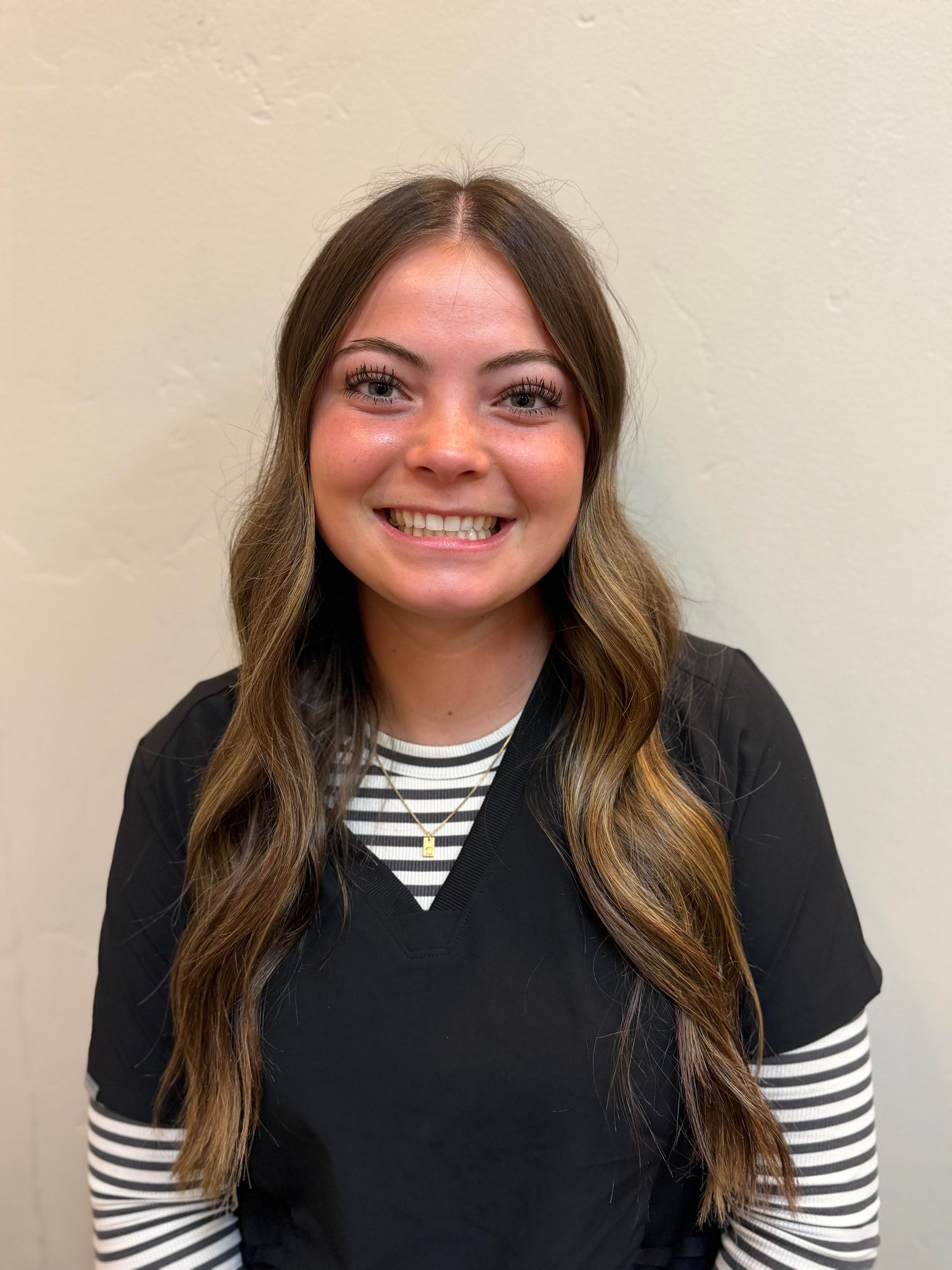 Blonde-haired person smiling, wearing a black shirt and a beaded necklace.
