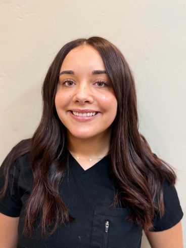 Woman with dark wavy hair smiling, wearing a black top against a beige wall.