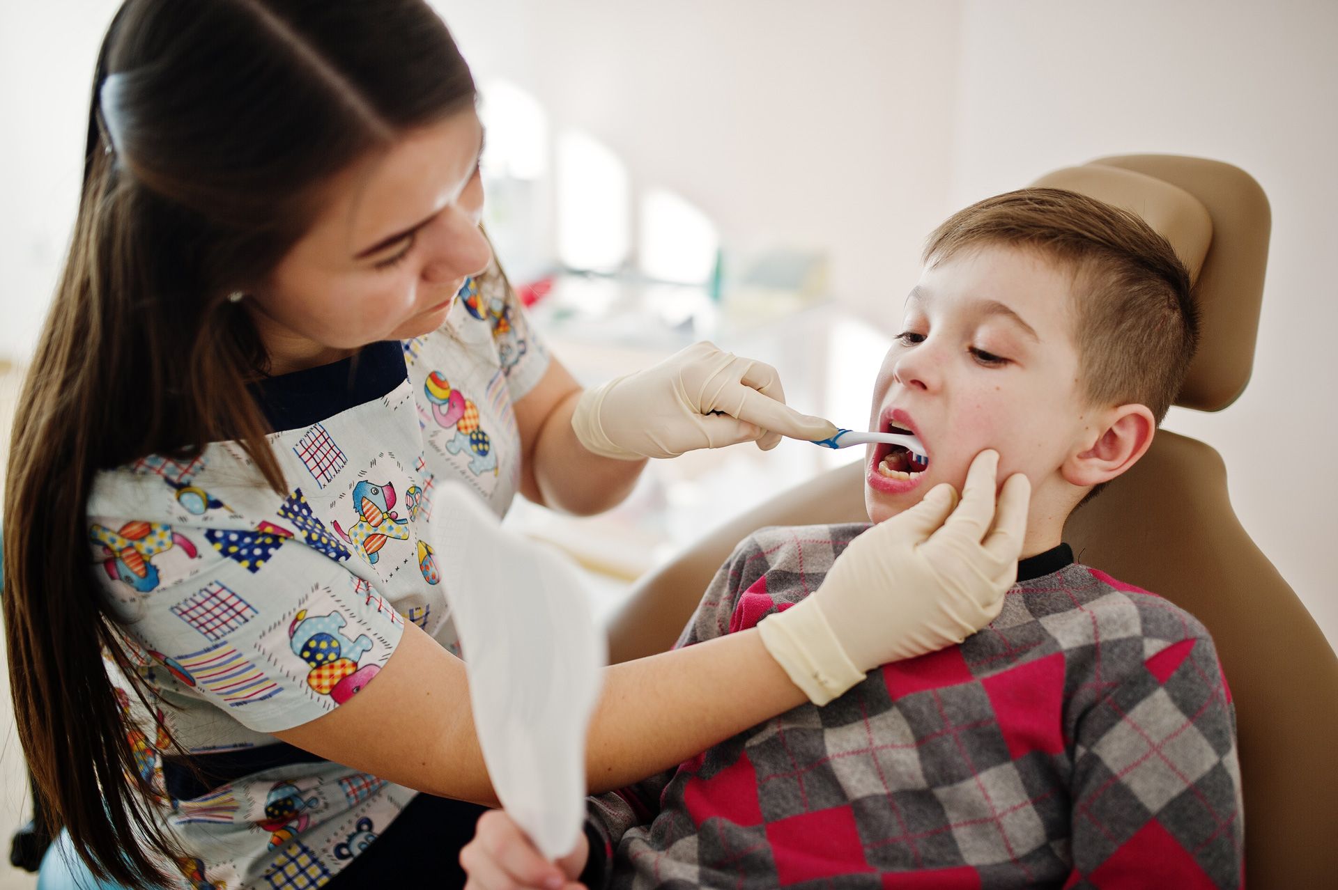 Dentist brushing a child's teeth in a dental office.