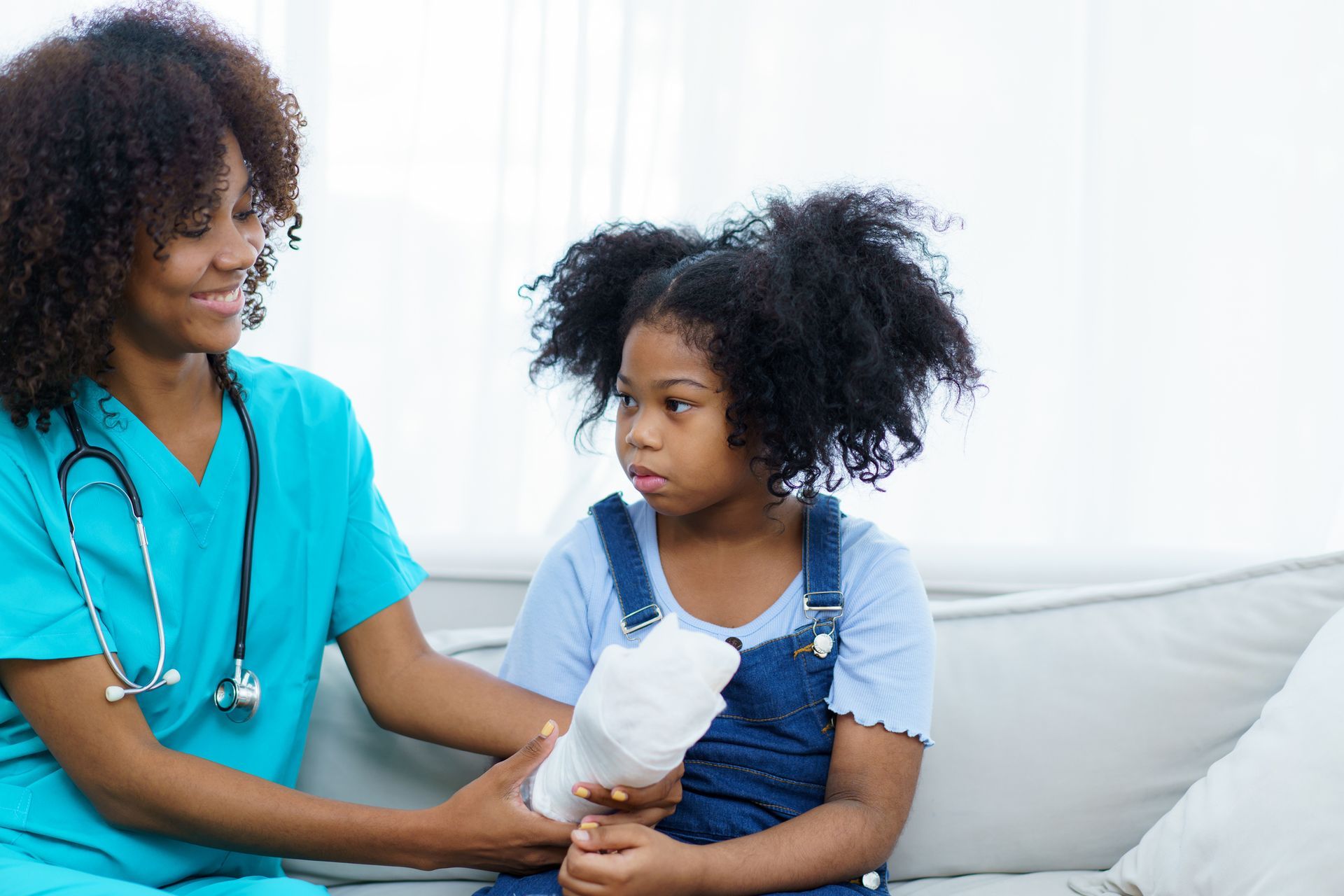 A nurse is holding the hand of a little girl who is sitting on a couch.