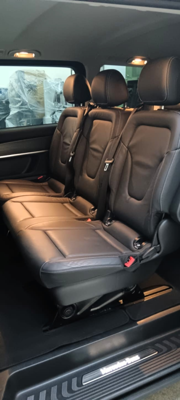 Interno di un veicolo di lusso che mostra tre sedili in pelle nera disposti in fila con cinture di sicurezza e una soglia della portiera con il logo Mercedes-Benz.