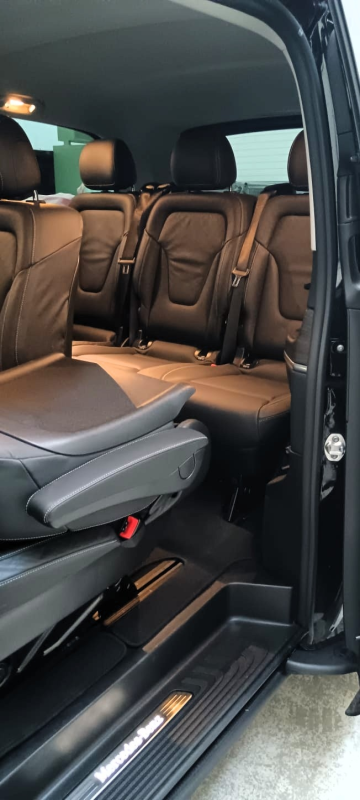 Uno scorcio dell'interno di un veicolo con sedili passeggeri in pelle marrone scuro e soglia della portiera illuminata.