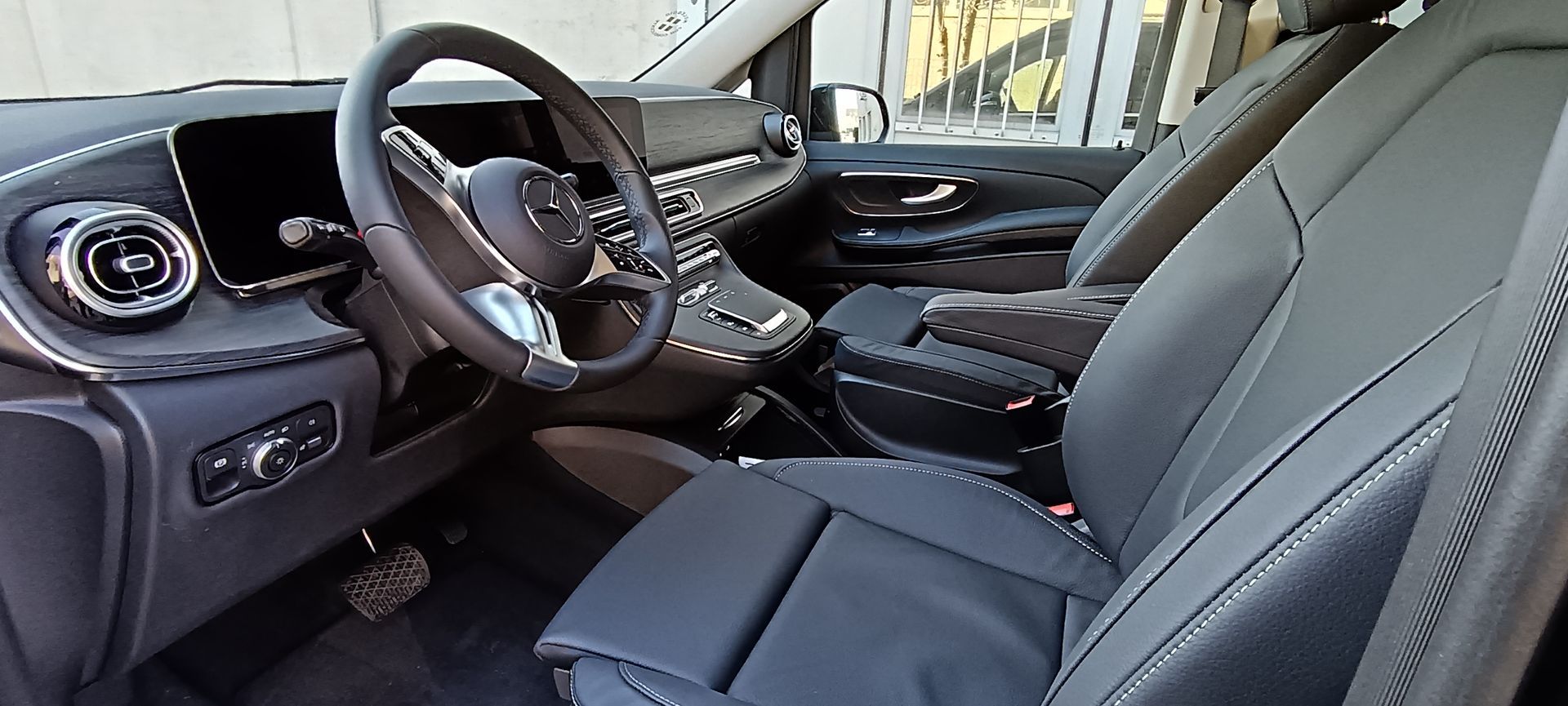 Interno di un veicolo con volante, cruscotto, sedili in pelle scura e console centrale.