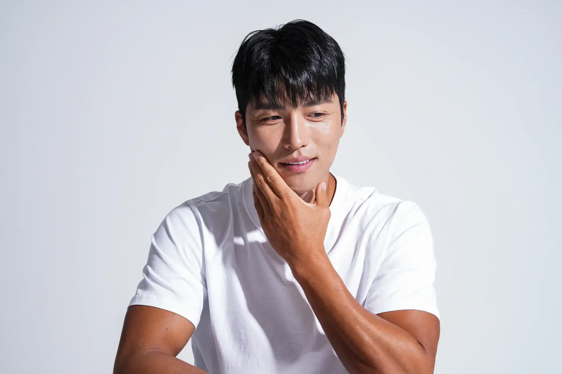 Person in a white shirt touching their chin, looking thoughtful against a light gray background.