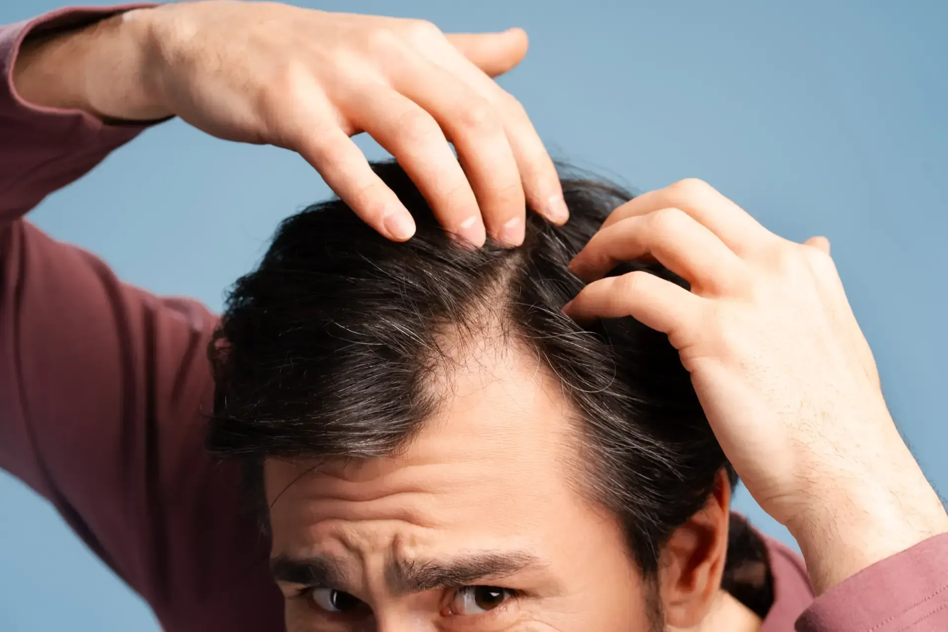 Man checking his thinning hair with both hands against a blue background