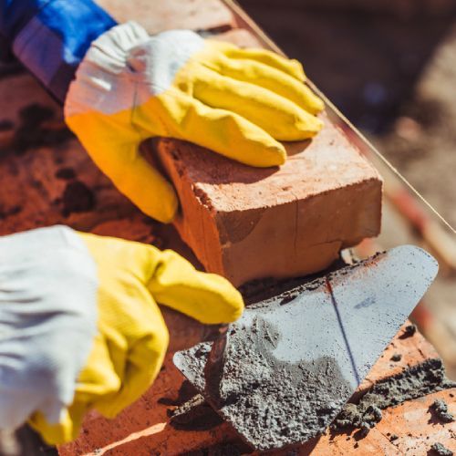 Una persona que lleva guantes amarillos está trabajando en una pared de ladrillos.