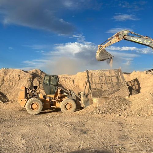 Una excavadora está cargando tierra en un cucharón en un campo de tierra.