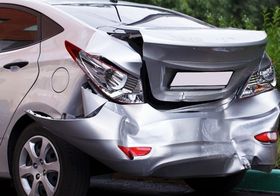 a silver car with a damaged bumper is parked on the side of the road .