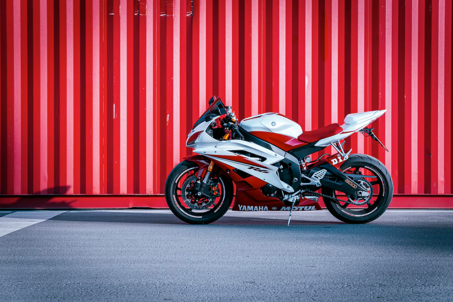 A red and white motorcycle is parked in front of a red and white striped wall.