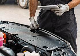 A mechanic is looking at a tablet while working on a car.