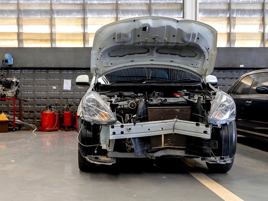 A car is being repaired in a garage with the hood open.