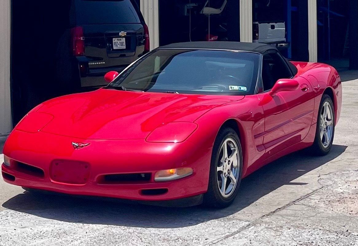 A red corvette convertible is parked in front of a garage.