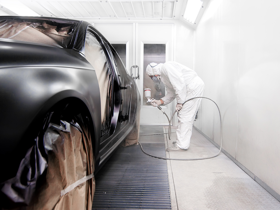 A man is painting a car in a paint booth.