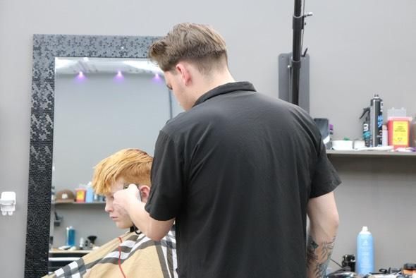 A man is getting his hair cut by a barber in front of a mirror.