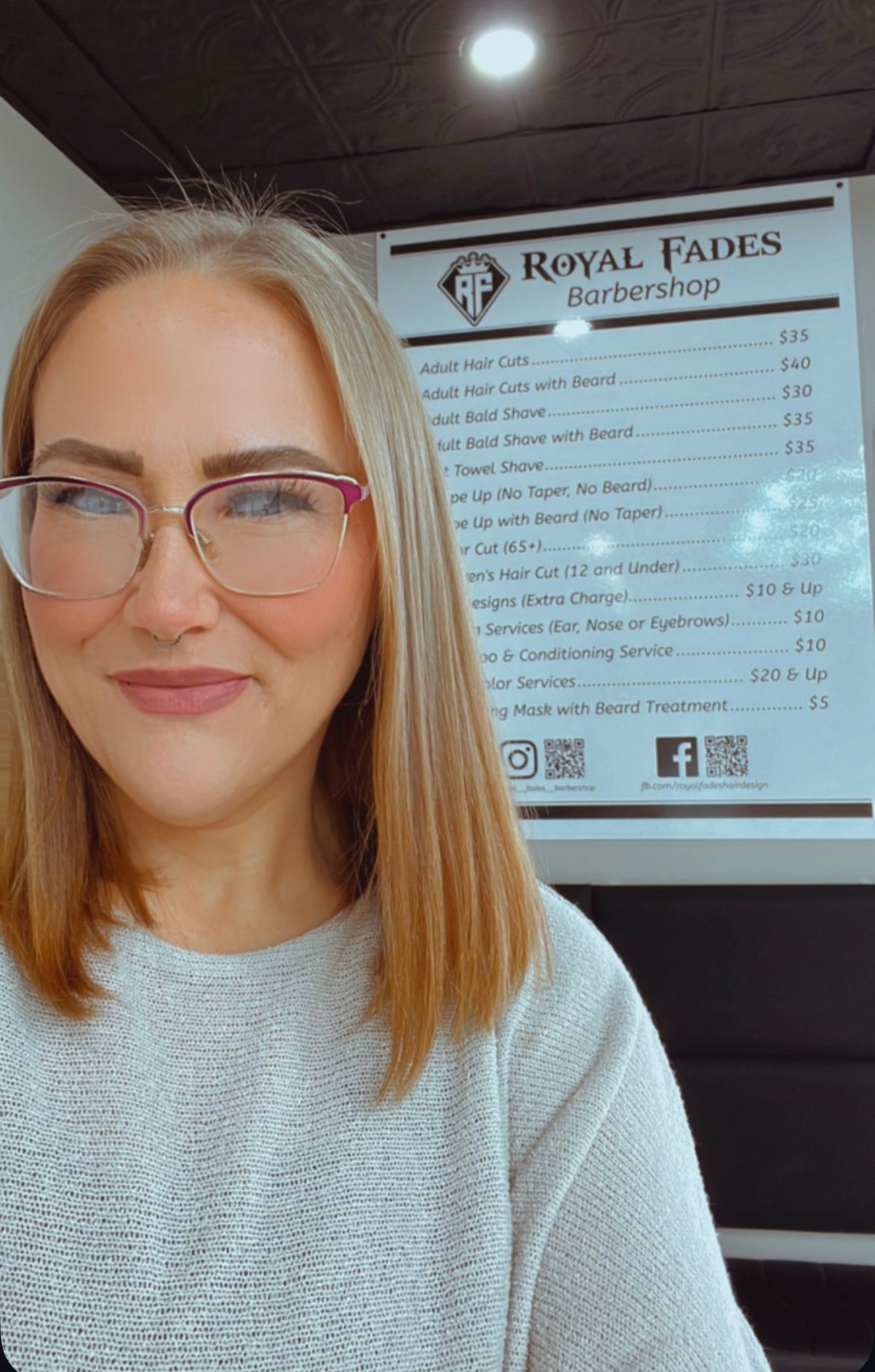 A woman wearing glasses is standing in front of a menu at a barber shop.