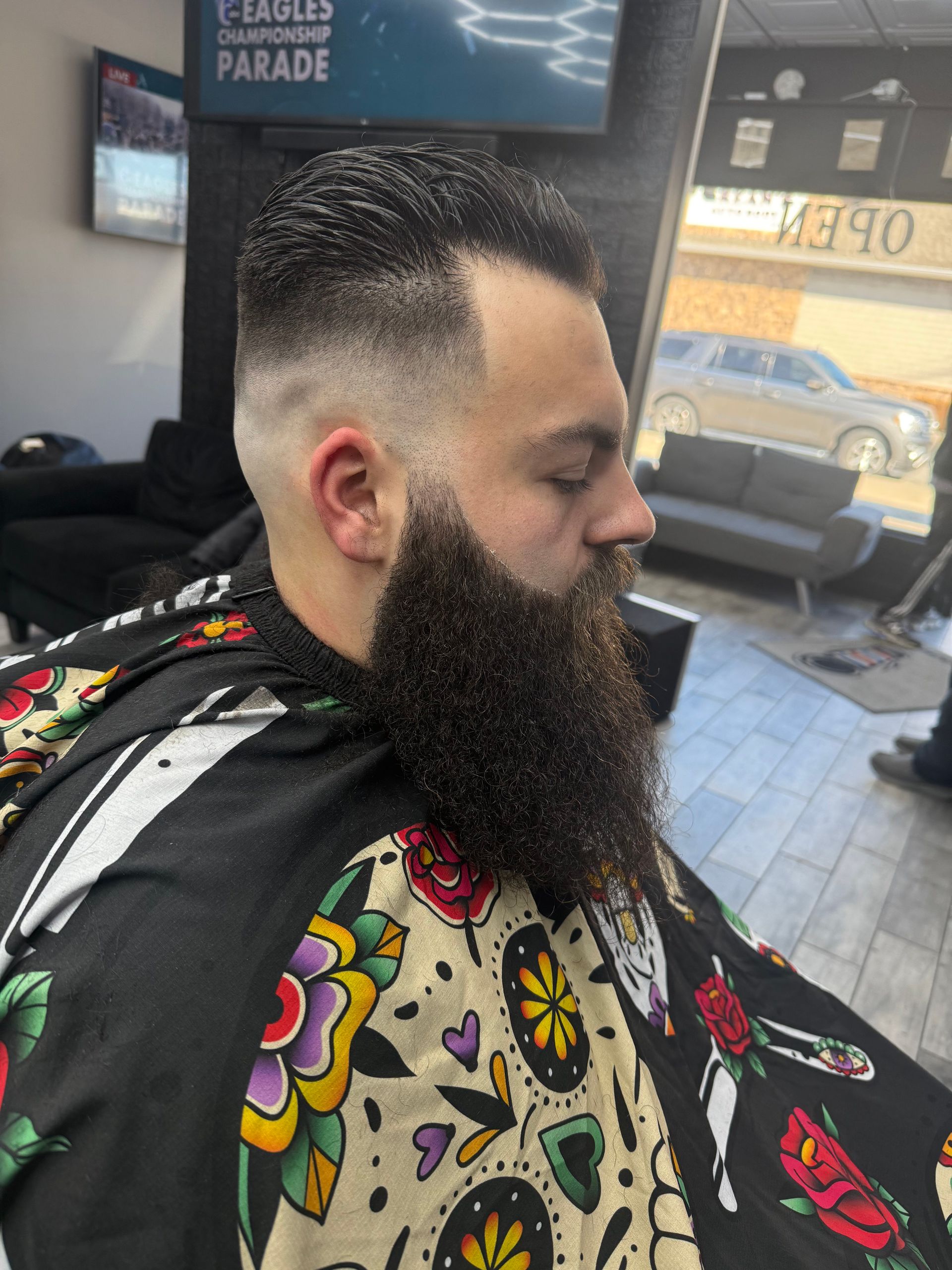 A man with a beard is getting his hair cut at a barber shop.