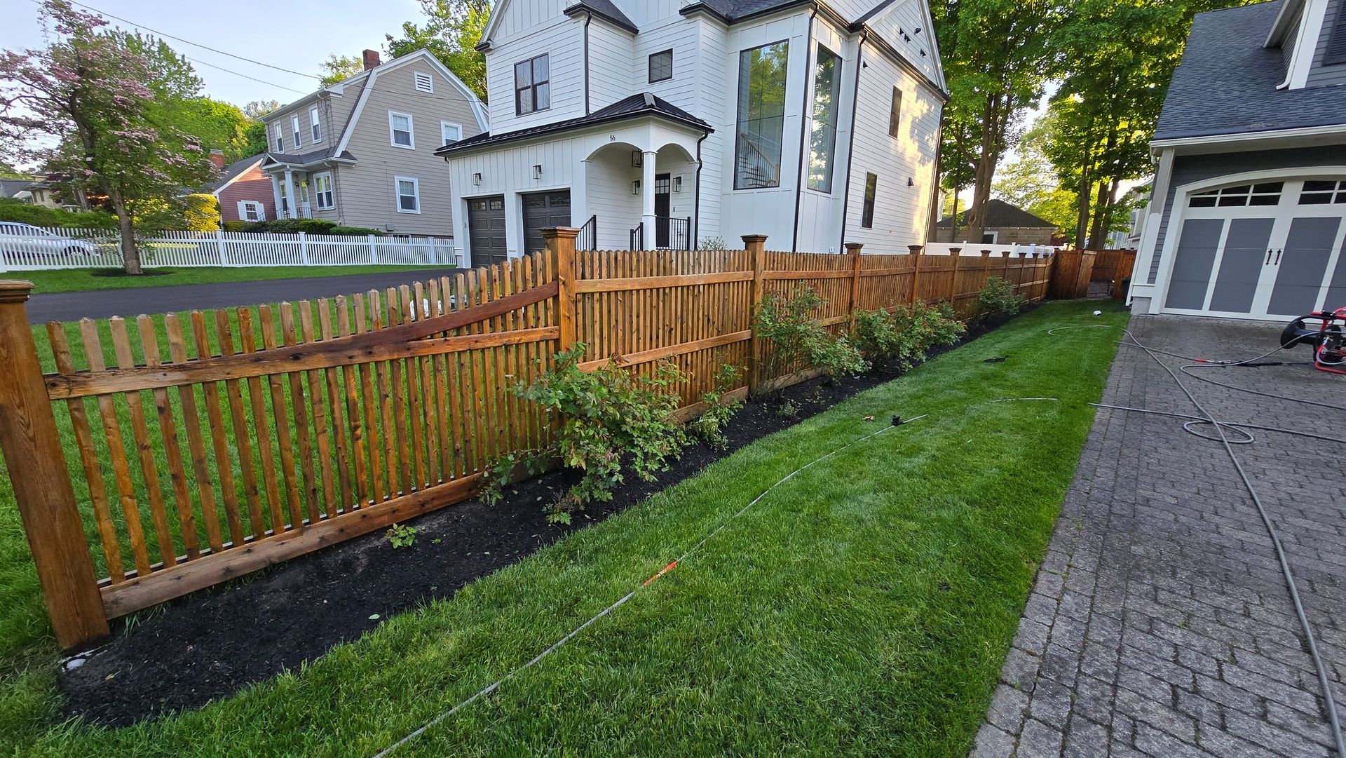 A wooden fence surrounds a lush green yard in front of a white house.