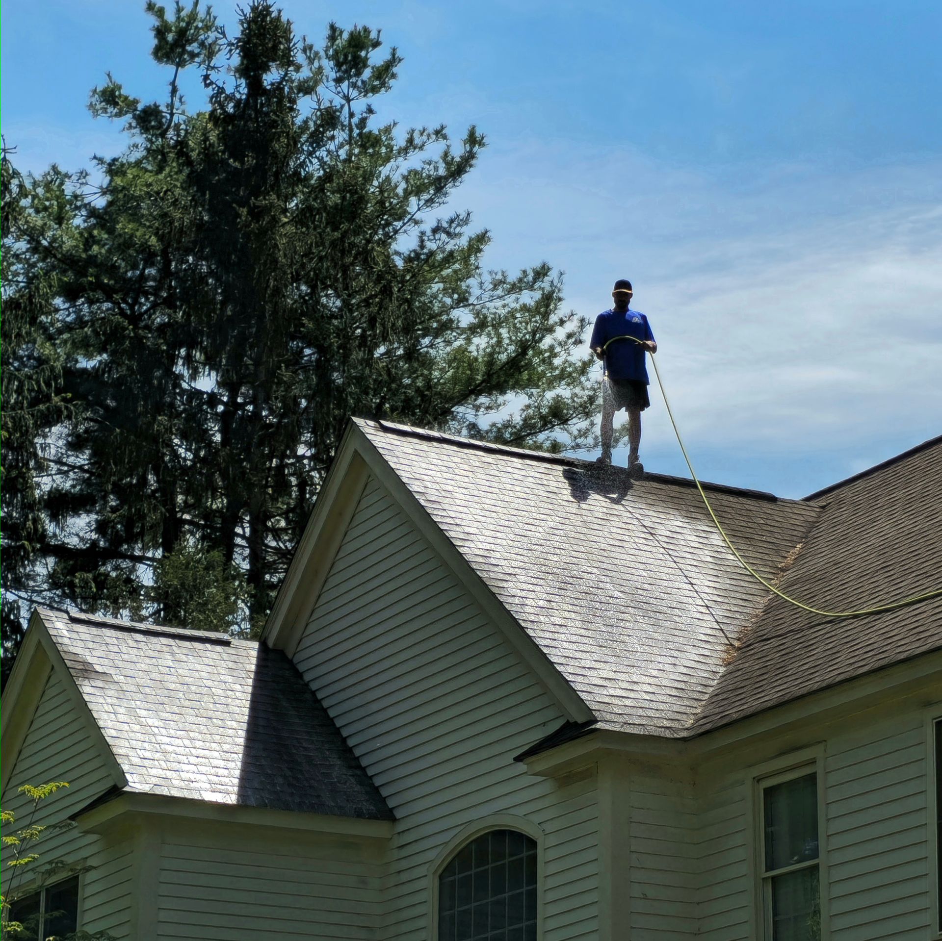A man in a blue shirt is standing on the roof of a house