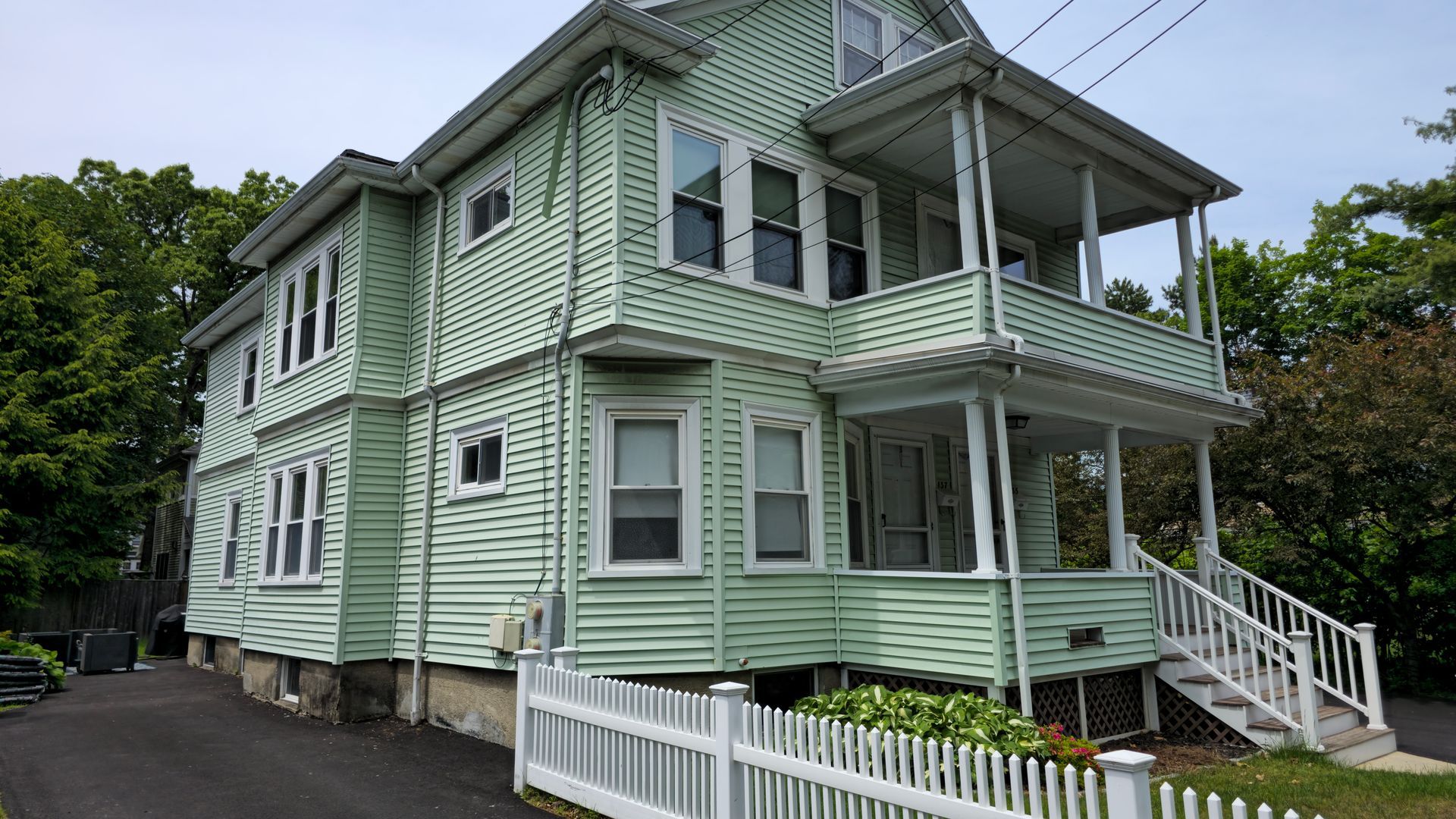 A large green house with a white picket fence in front of it.