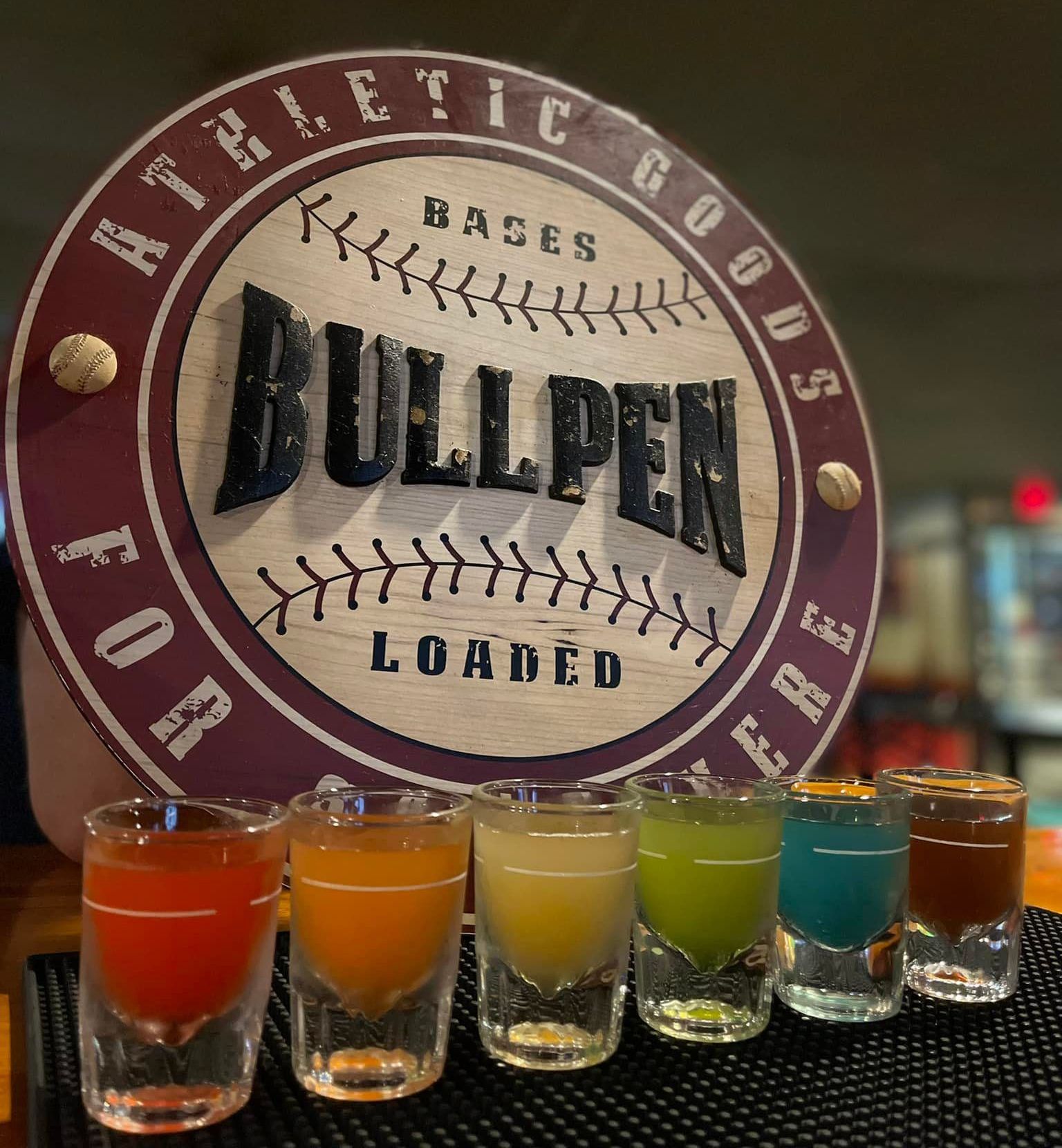 A bunch of shot glasses are sitting on a bar next to a sign that says bullpen loaded