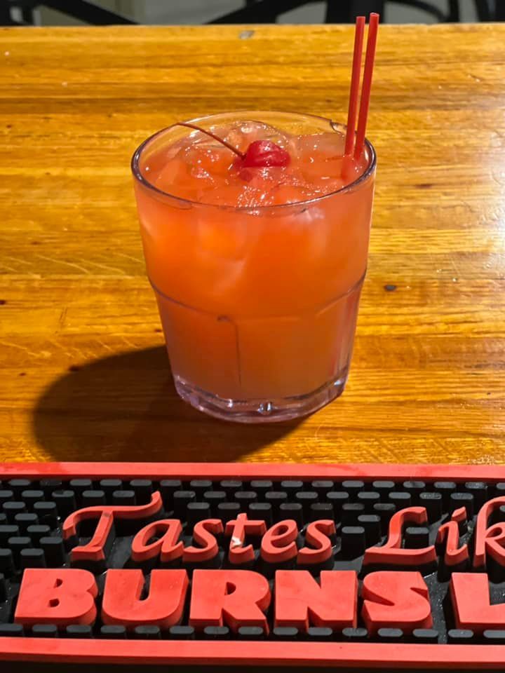 A glass of orange juice with a cherry on top is on a wooden table.