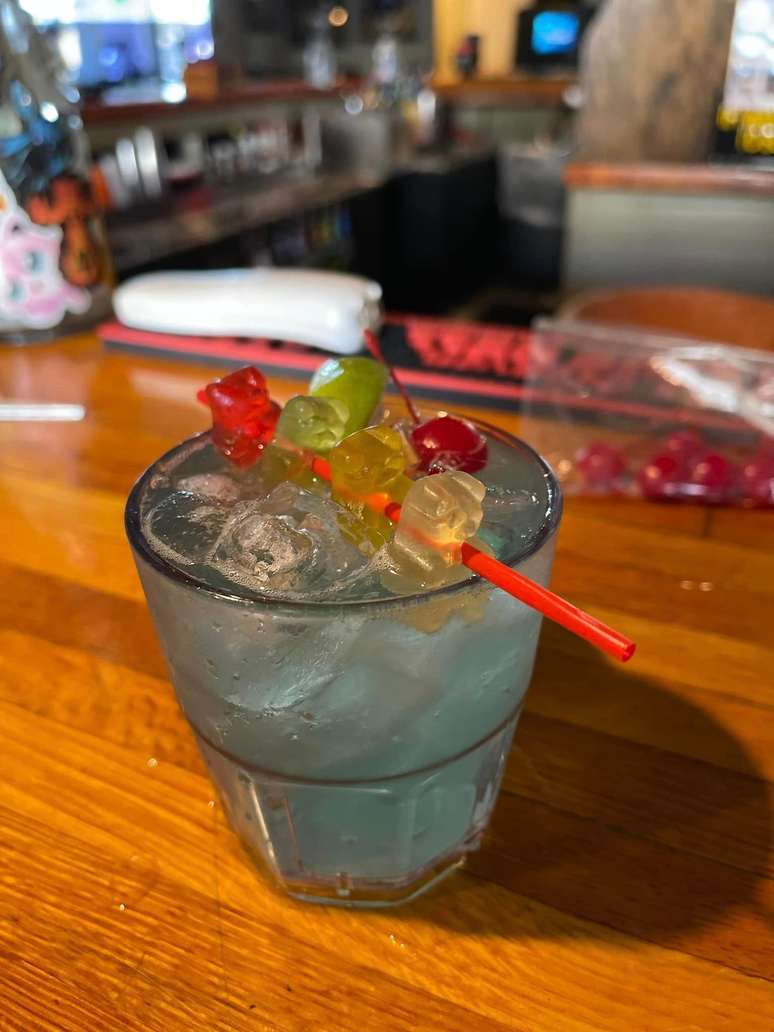A glass of iced water with gummy bears and cherries on a bar.