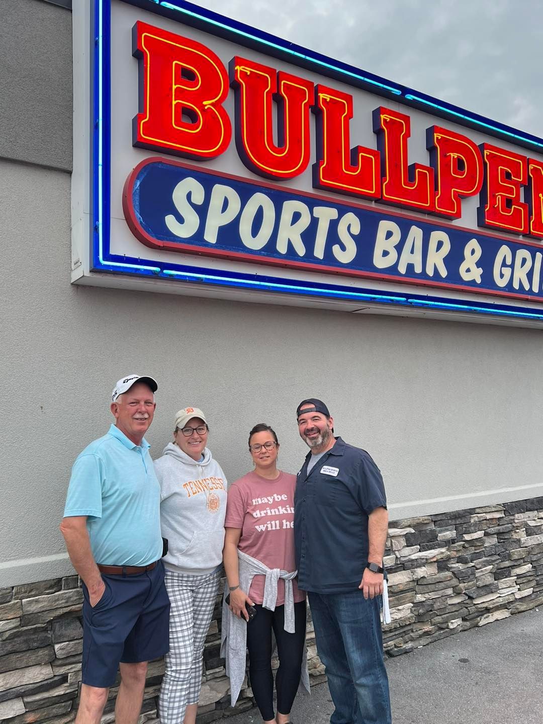 A group of people standing in front of a bullpen sports bar and grill sign