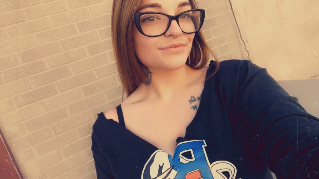 A woman wearing glasses is taking a selfie in front of a brick wall.