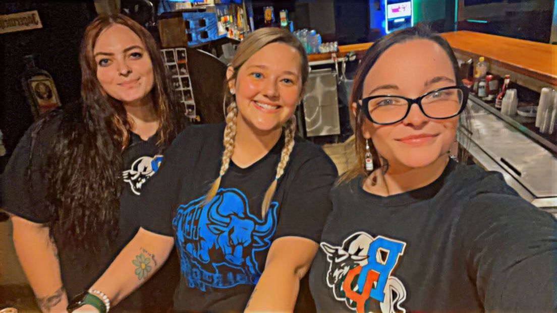 Three women are posing for a selfie in a bar.