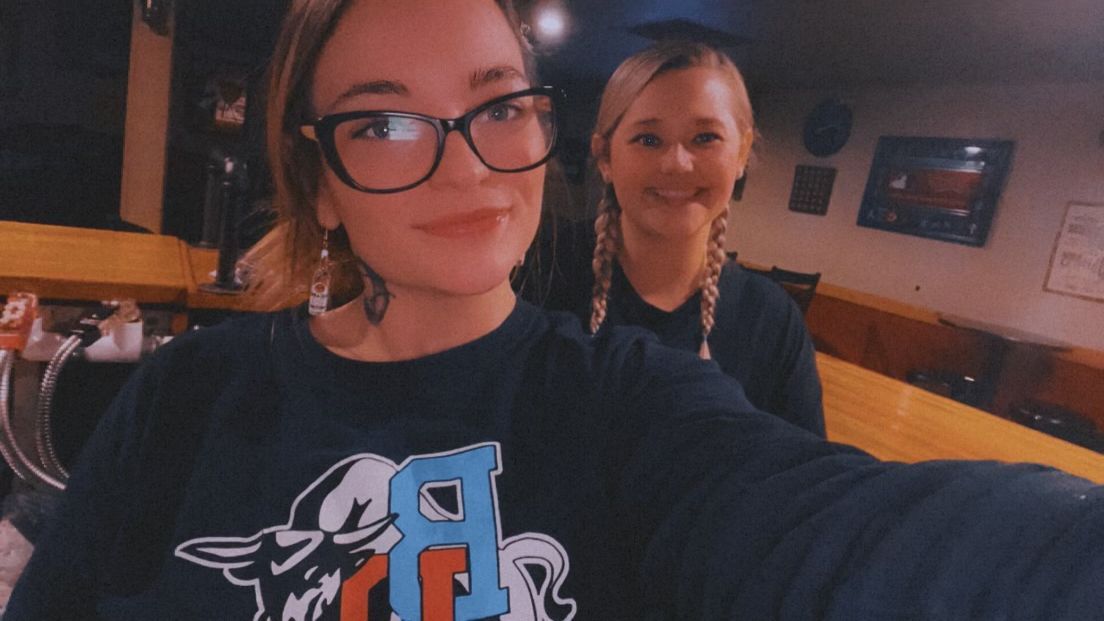 Two girls are taking a selfie in a restaurant . one of the girls is wearing glasses.