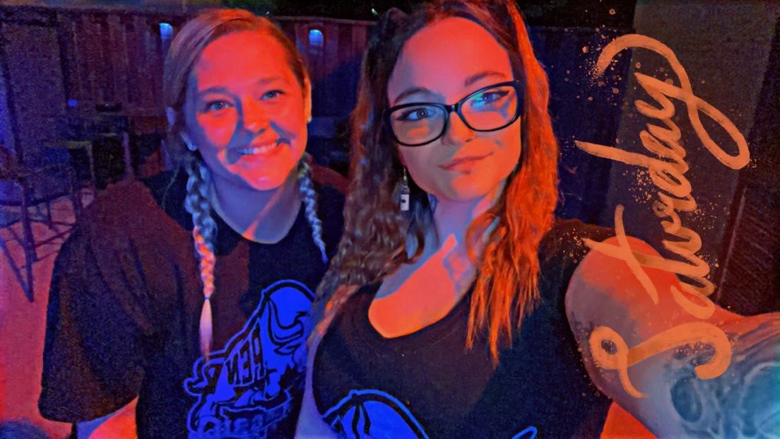 Two women are posing for a picture in front of a sign that says saturday.