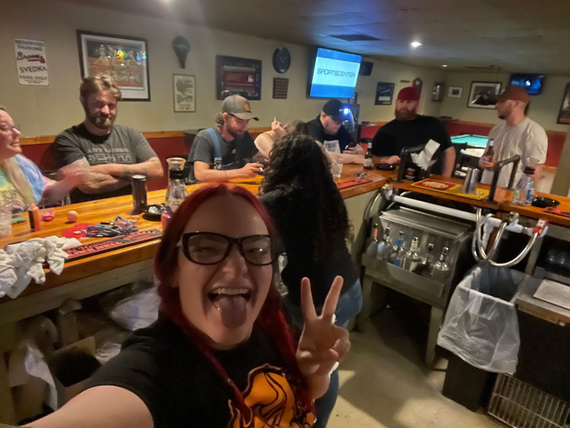 A woman is taking a selfie in a bar with her tongue out.