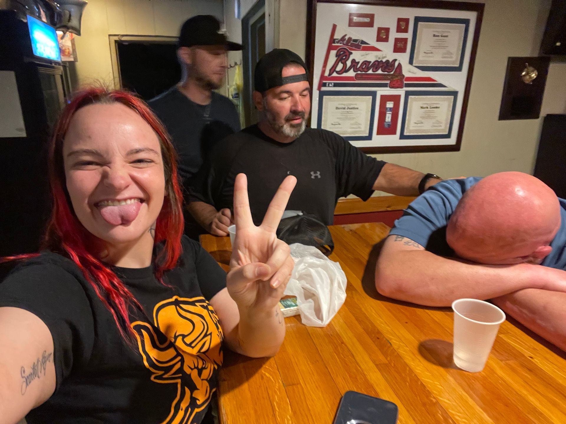 A group of people are sitting at a table and one of them is giving a peace sign.