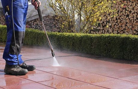 A man is using a high pressure washer to clean a tiled floor.