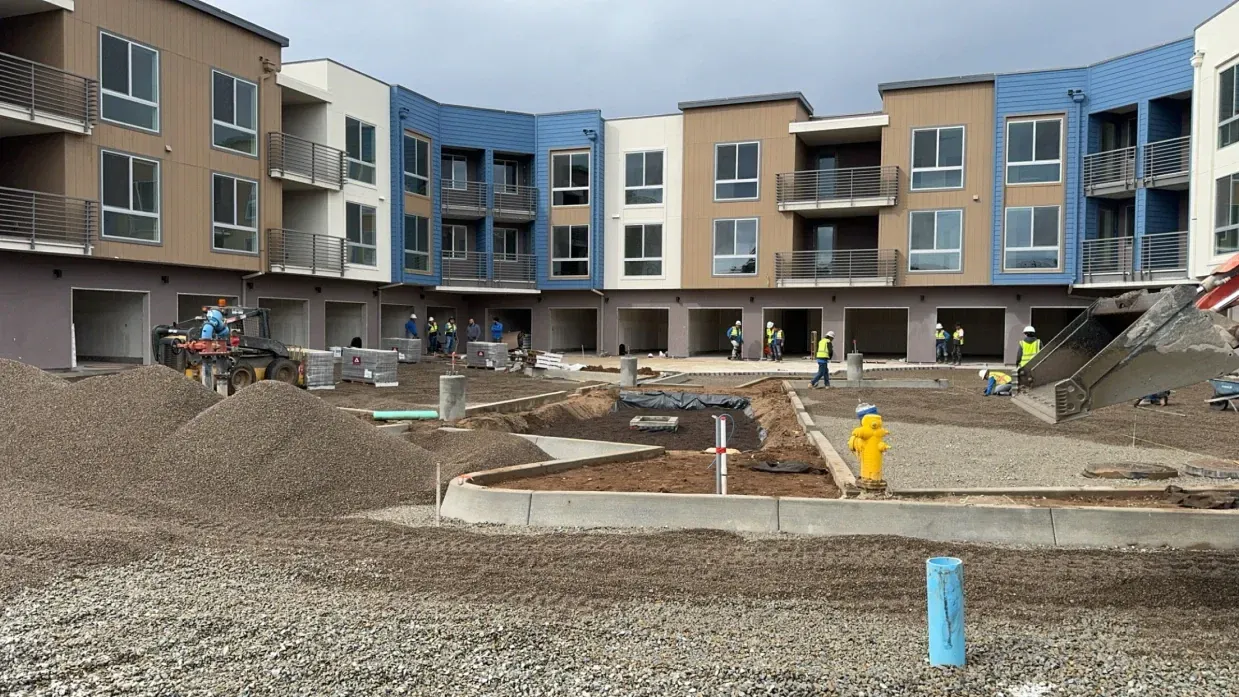 Construction site with apartment building, workers, and gravel.