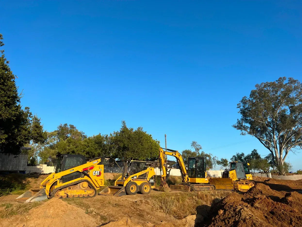 Construction site with yellow earthmovers excavating under a blue sky.