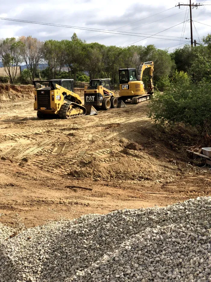 Construction site with three CAT machines: excavator, skid steer, and compact track loader.