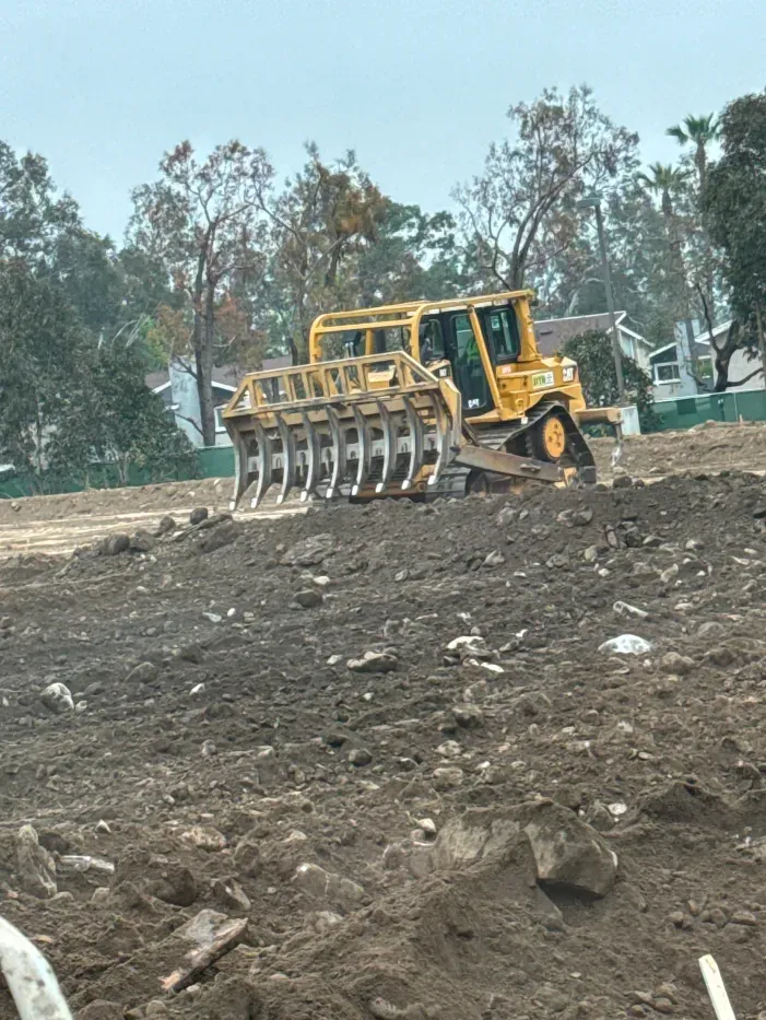 Yellow bulldozer with rake attachment clearing dirt on a construction site.