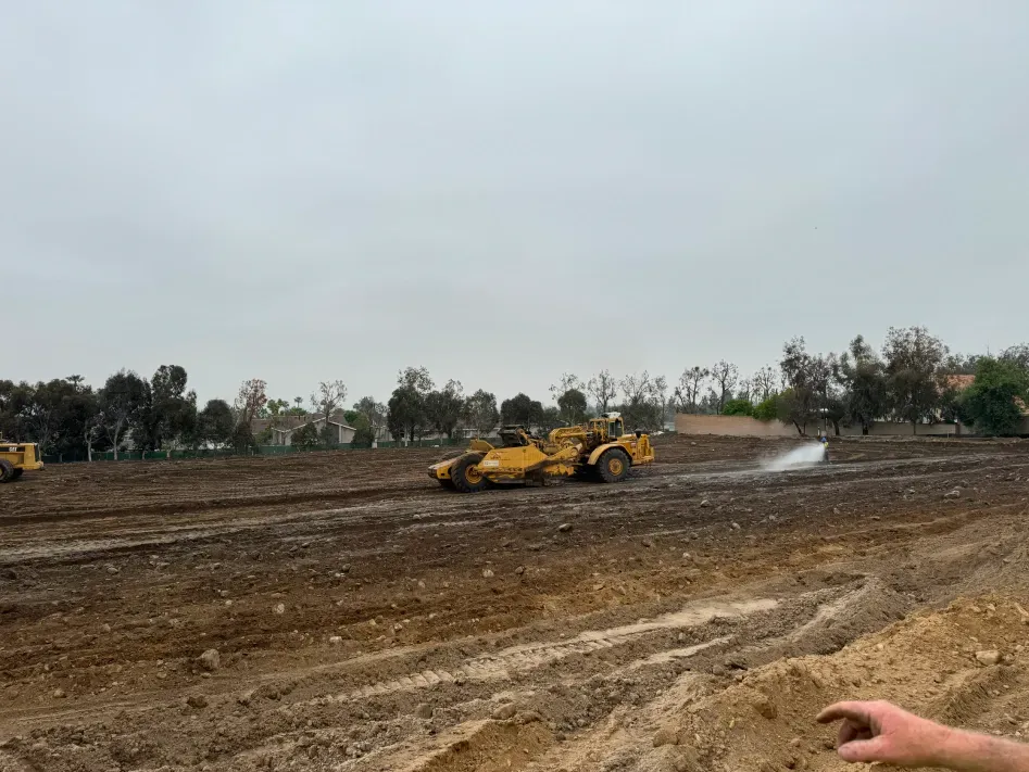 Yellow earth-moving machine on muddy ground. Trees in the background under an overcast sky.