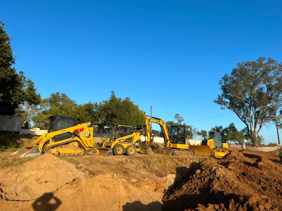 Construction site with yellow heavy machinery on a brown dirt pile under a clear blue sky.