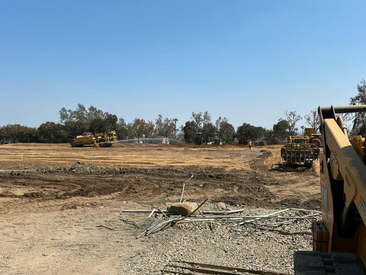 Construction site with heavy machinery, including bulldozers, clearing land under a blue sky.