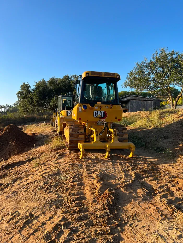 Yellow CAT bulldozer on dirt path, clear blue sky in background.