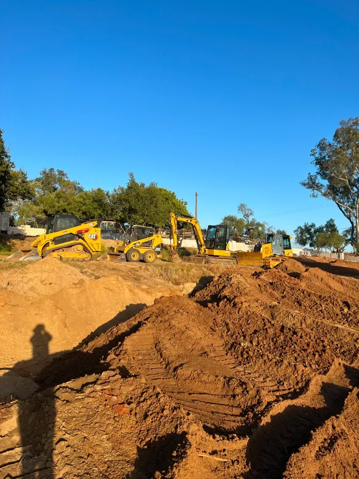 Construction site with several yellow excavators and piles of dirt under a blue sky.