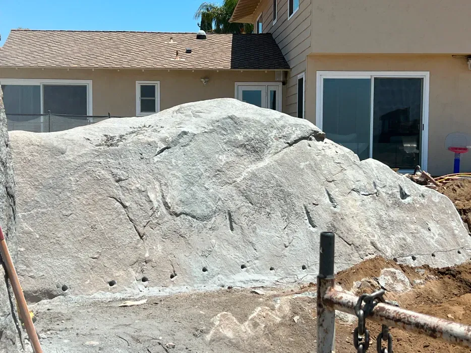 Large gray rock formation next to a tan building under construction.