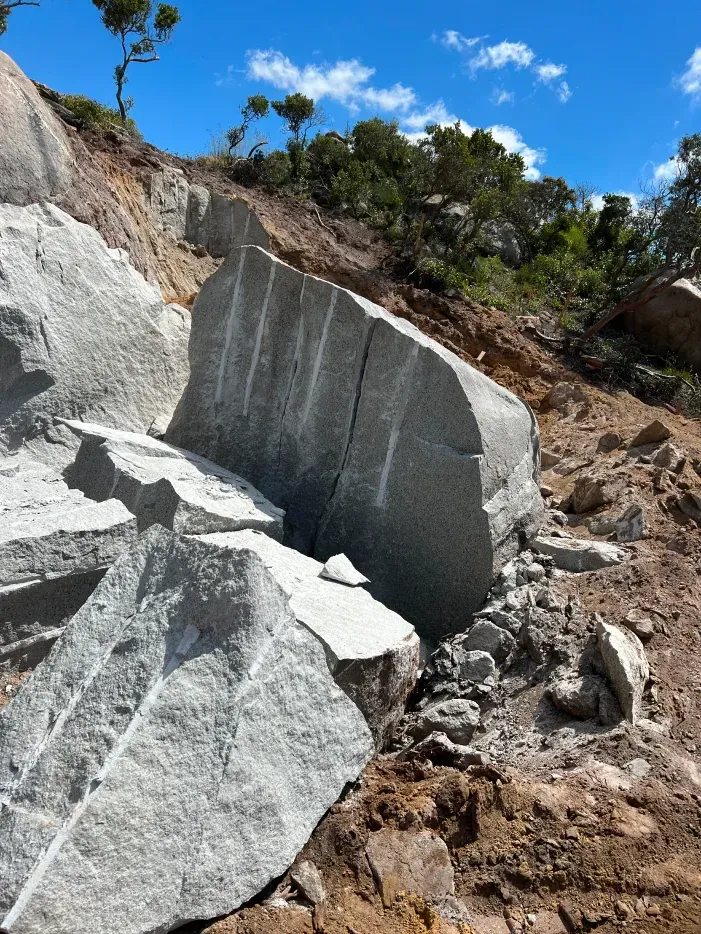 Large gray rock formation cut into blocks on a hillside; sunny day.