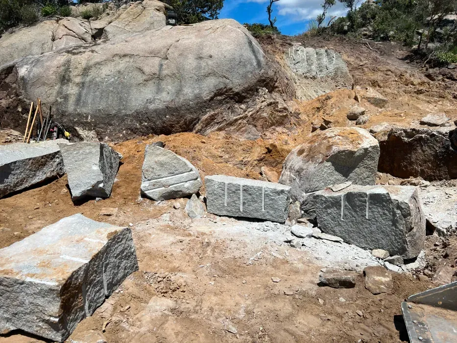 Construction site with heavy machinery, sunlight, and a hillside in the background.