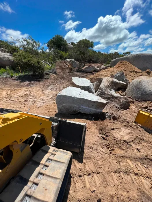 Tractor grading a dirt road in a rural setting under a blue sky, with a man operating it.