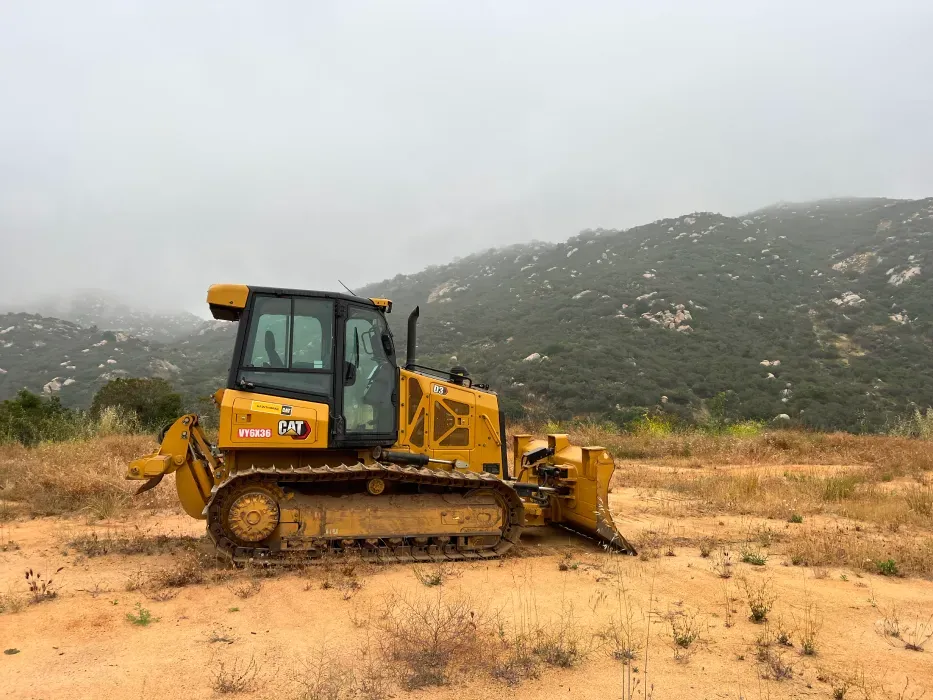 Yellow bulldozer on a dusty hillside, foggy mountain background.