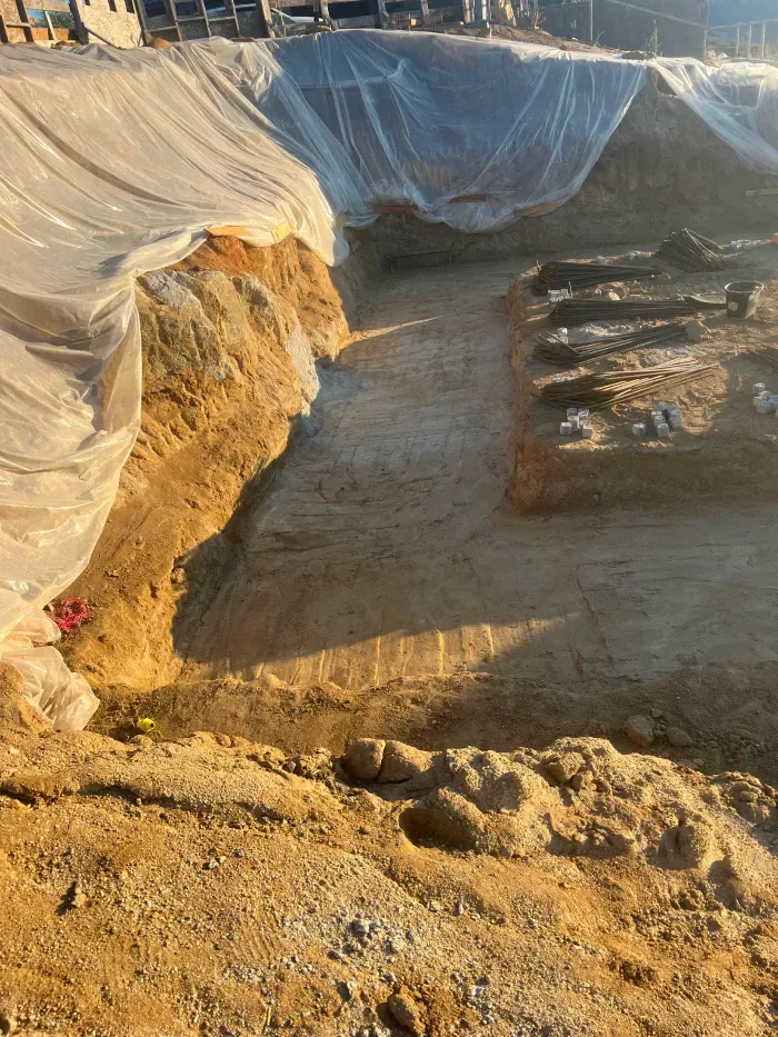 Construction site: Excavated earth covered by plastic sheeting. Building in the background.