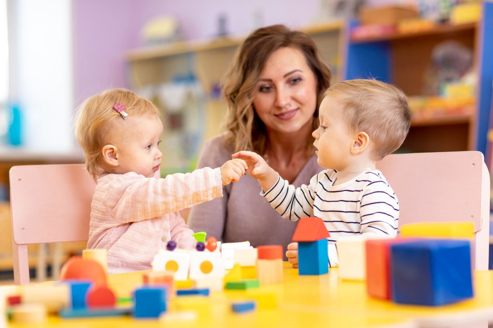 A woman is playing with two babies at a table with toys.
